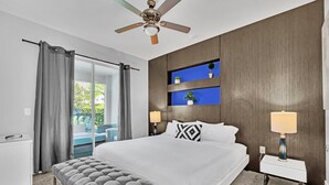 A modern hotel room with a large bed, a ceiling fan, a bench, a nightstand with a lamp, and a view of the outdoors through a sliding door. - 8BR Modern Villa • Games&Movie Room • Near Disney (Kissimmee)