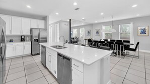 A modern kitchen with white cabinetry, a stainless steel refrigerator, and a dishwasher. - 8BR Modern Villa • Games&Movie Room • Near Disney (Kissimmee)