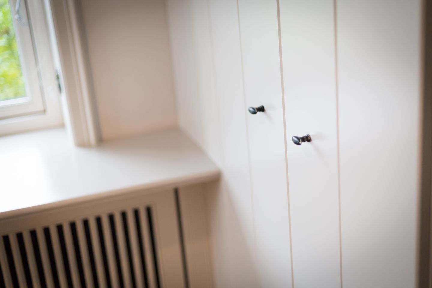 Ein weißer Kleiderschrank mit zwei schwarzen Knöpfen, einem Fenster und einem Lüftungsgitter.