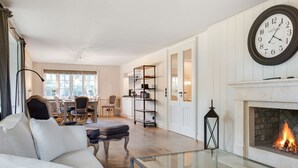 A living room with a white sofa, a glass coffee table, a fireplace, and a large wall clock.