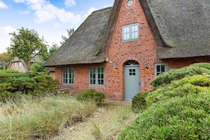 A traditional brick house with a thatched roof, a small porch, and a front door.
