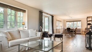 A spacious living room with a glass coffee table, a white sofa, and a dining area with a wooden table and chairs.