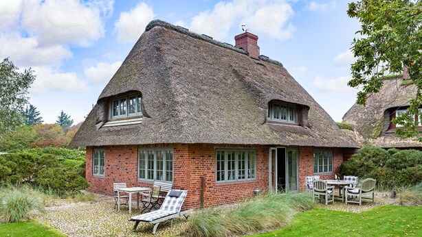 A thatched-roof house with a brick exterior, a door, and a small garden with a table and chairs.