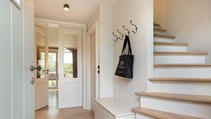 A hallway with a wooden staircase, a door with a handle, and a wall-mounted hook with a bag.