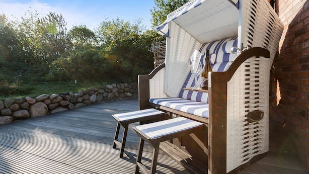 Une terrasse en bois avec un muret en pierre et une chaise en osier dotée de coussins à rayures.