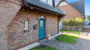 Une maison en briques avec une porte bleue, un petit porche et un mur en pierre.