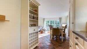 Une cuisine comprenant un coin repas, avec un meuble blanc doté de nombreuses étagères et tiroirs, un sol carrelé et une fenêtre laissant entrer la lumière naturelle.