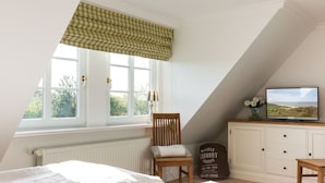 Une chambre avec une grande fenêtre, un lit, une chaise, un téléviseur et un meuble.