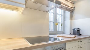 Moderni keittiö, jossa on sisäänrakennettu induktioliesi, kahvinkeitin ja ikkuna, jossa on verhot.