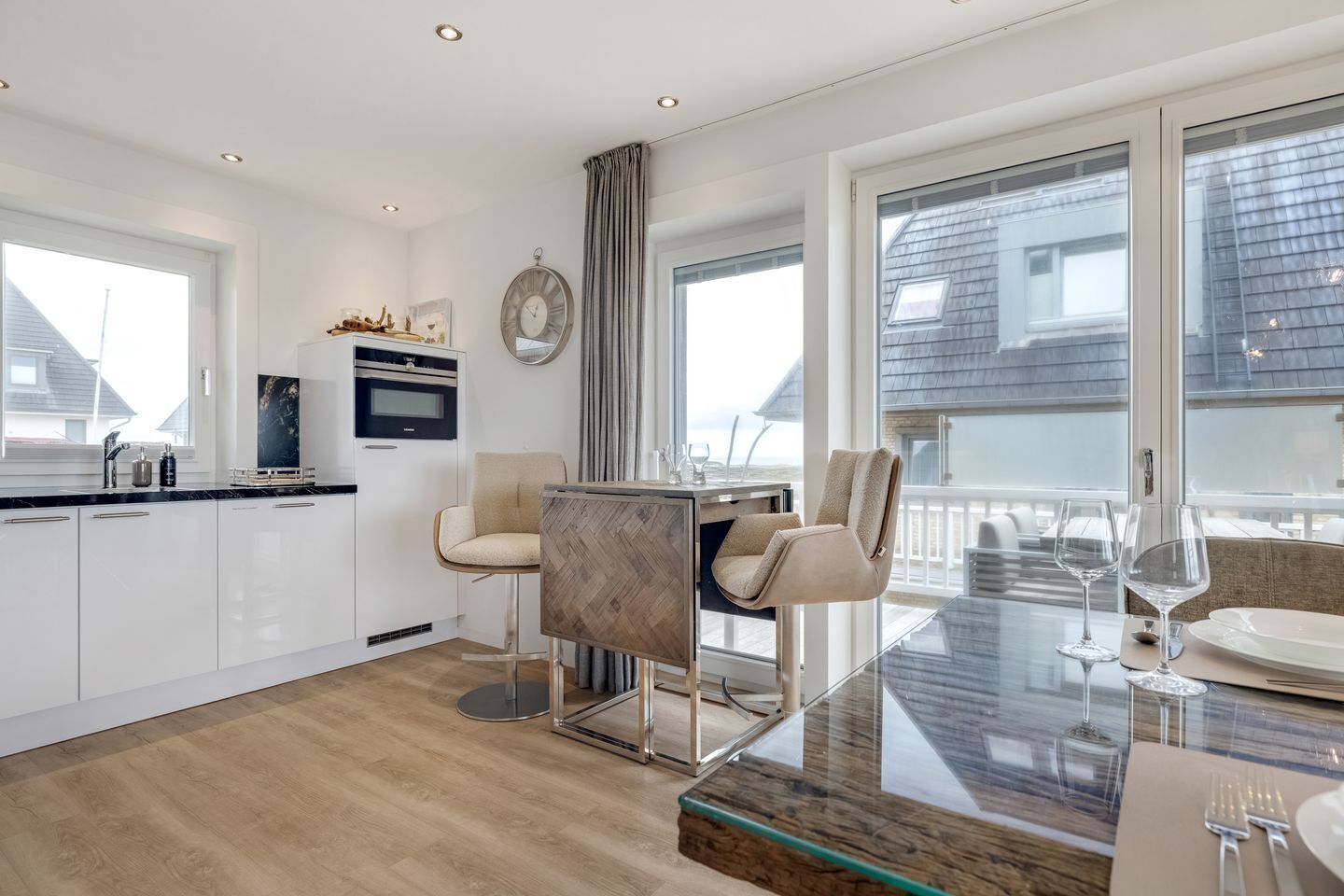 A modern kitchen with white cabinets, a built-in oven, and a dining area with a glass table and chairs.