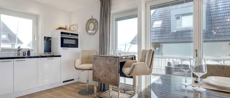 A modern kitchen with white cabinets, a built-in oven, and a dining area with a glass table and chairs.