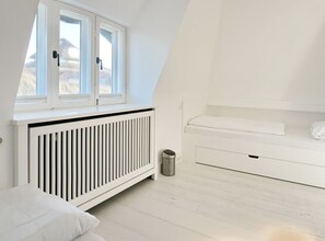 Ein Zimmer mit schrägem Dach, Heizkörper, Bett, Fenster und einer weißen Kommode.