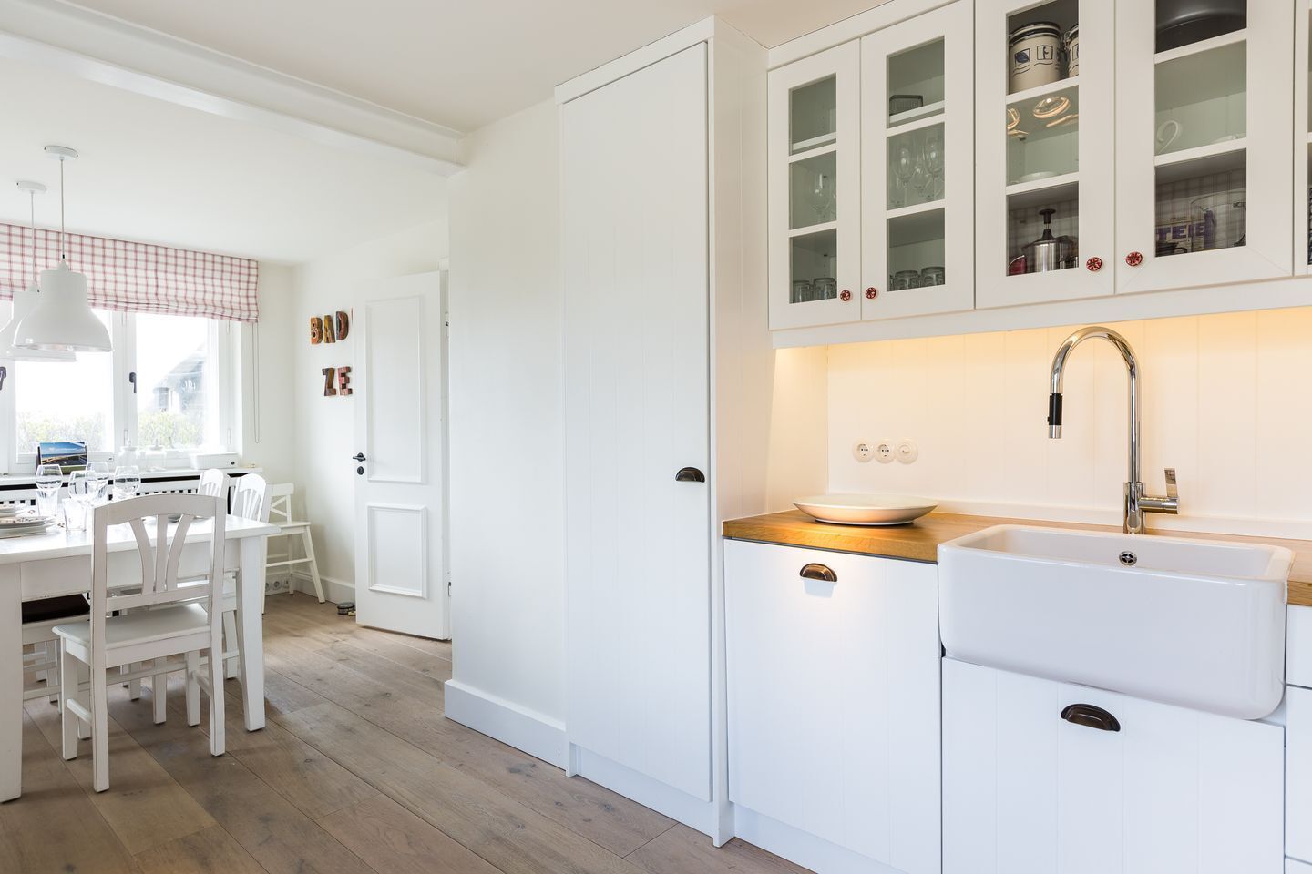 A kitchen with white cabinets, a wooden countertop, a sink, and a dining area with chairs.