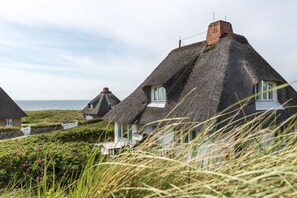 Ferienhäuser mit Strohdach, weißen Fensterrahmen, einer Steinsäule und Blick auf das Meer.