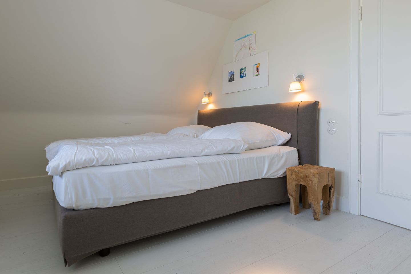 Ein Bett mit weißer Bettwäsche, ein Nachttisch aus Holz und Wandleuchten.