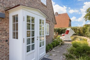 Een bakstenen huis met een witte voordeur, een dak met rode tegels, en een tuin met een barbecue en buitenmeubilair.