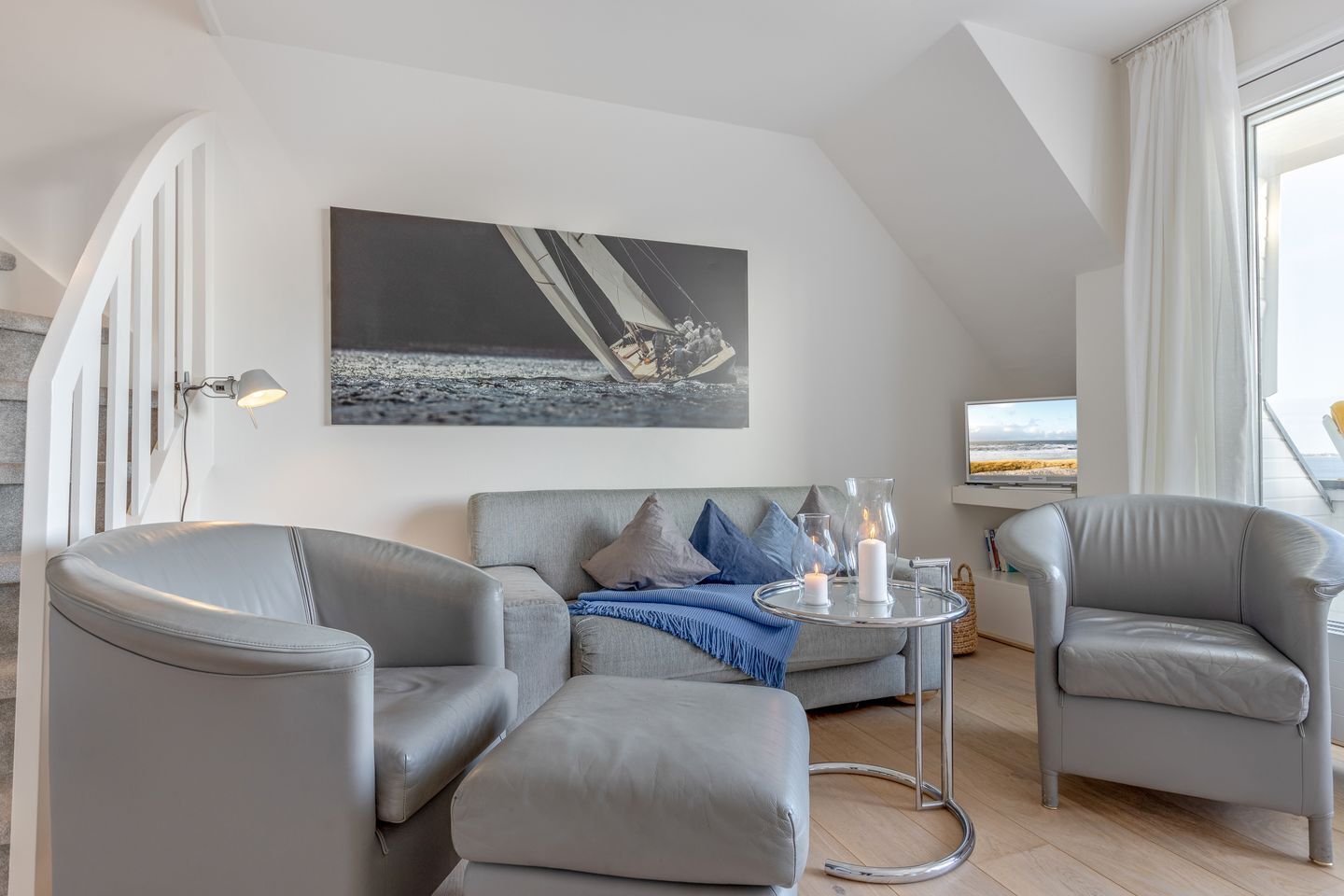 A modern living room with a grey sofa, two armchairs, a coffee table with candles, and a large painting on the wall.
