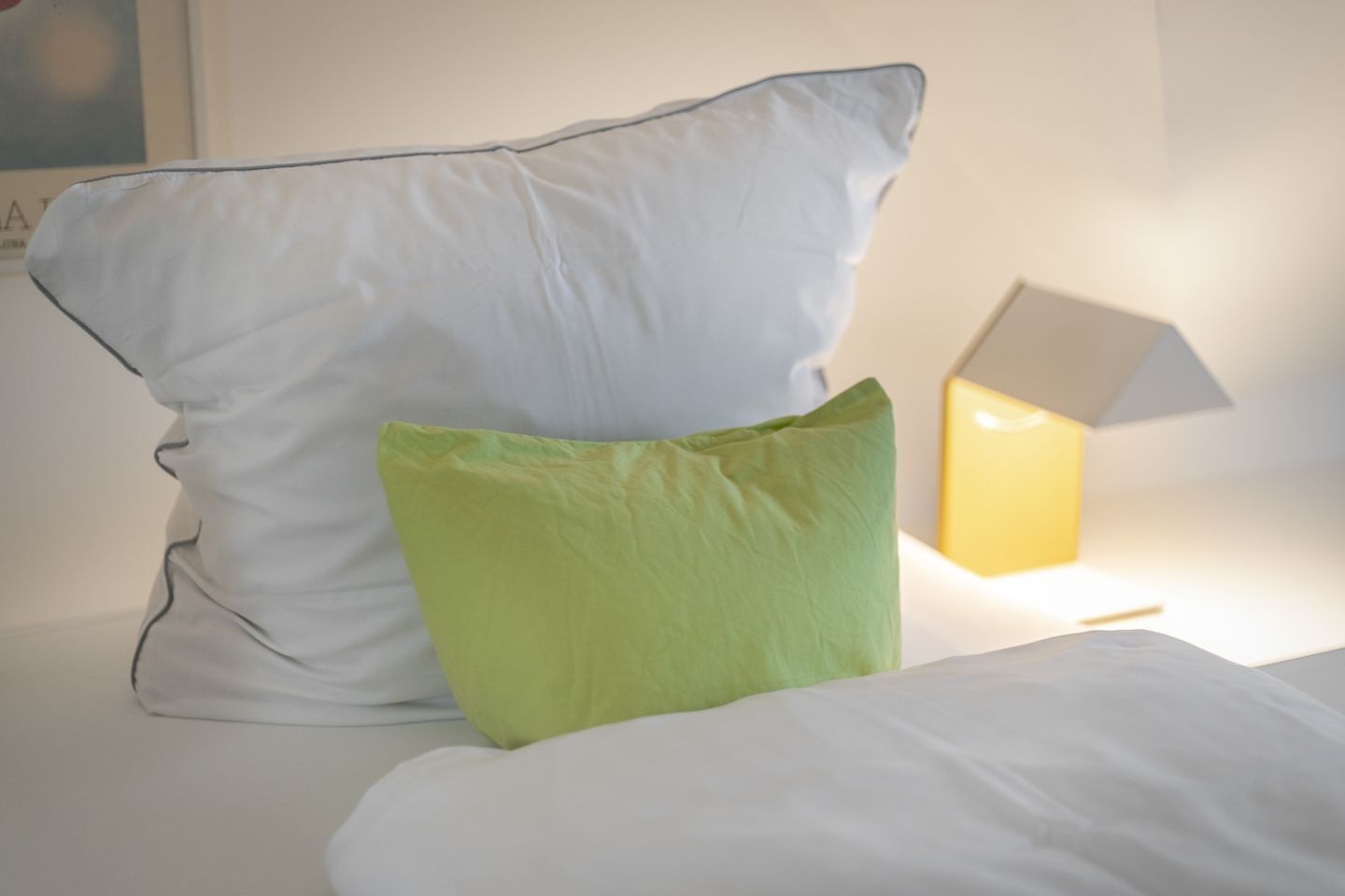 A bed with white bedding and two pillows, one white and one green, and a bedside lamp.