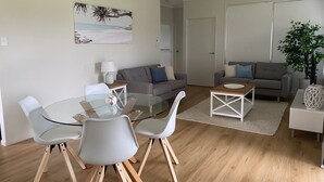 A modern living room with a glass dining table, grey sofas, and wooden flooring. - Rural Setting - Close to shops, Townsville Hospital and Riverway (Gumlow)