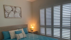 A bedroom with a bed, a nightstand with a lamp, a wall-mounted artwork, and a window with blinds. - Rural Setting - Close to shops, Townsville Hospital and Riverway (Gumlow)