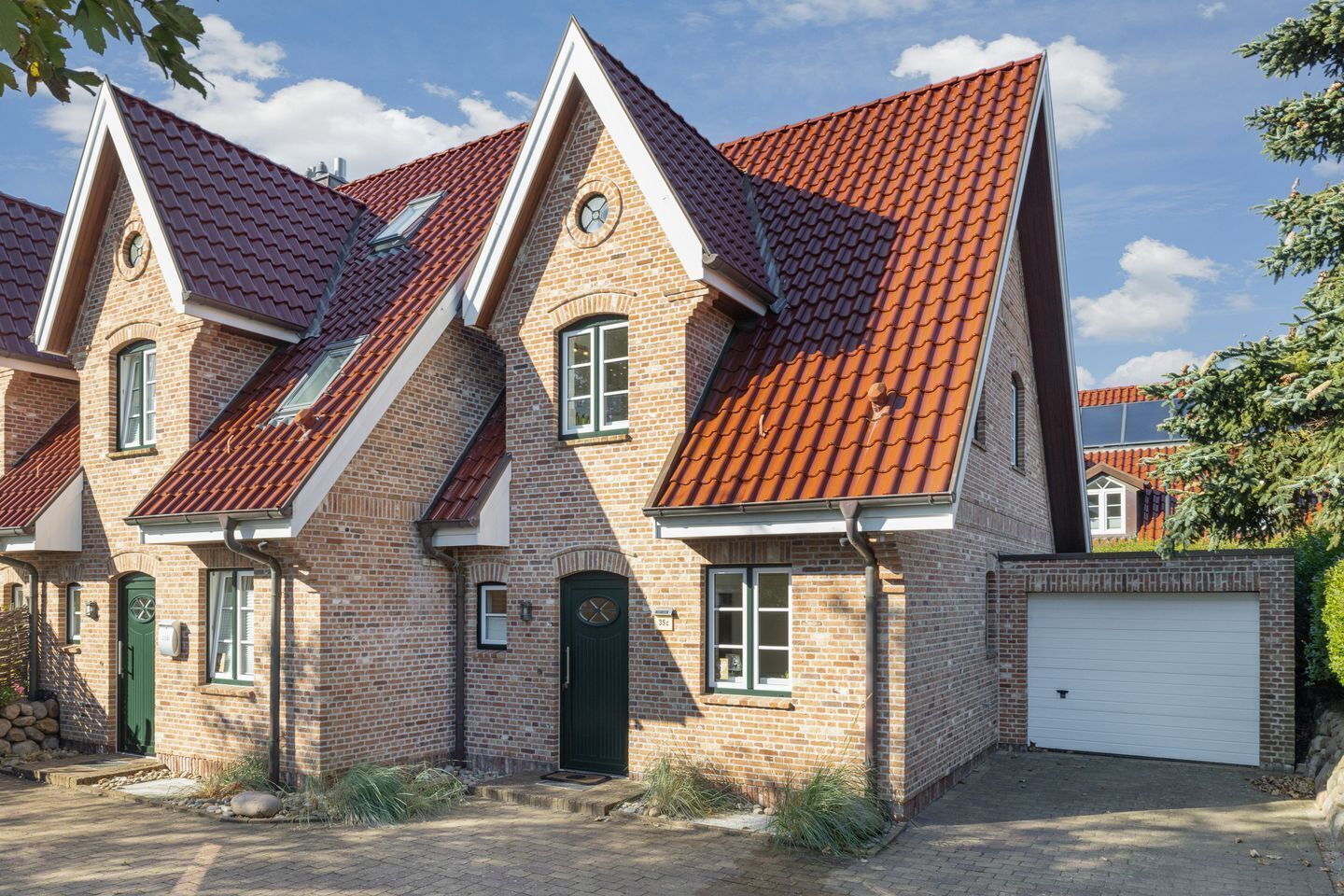 Een tweelaags bakstenen huis met een rode pannendak, een garage en een kleine voortuin.