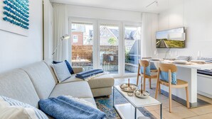 A modern living room with a sofa, chairs, a coffee table, and a TV. - Ringelgans - Urlaub im Herzen von Westerland, das Erleben Sie in dem Appartement Ringelgans (Sylt)