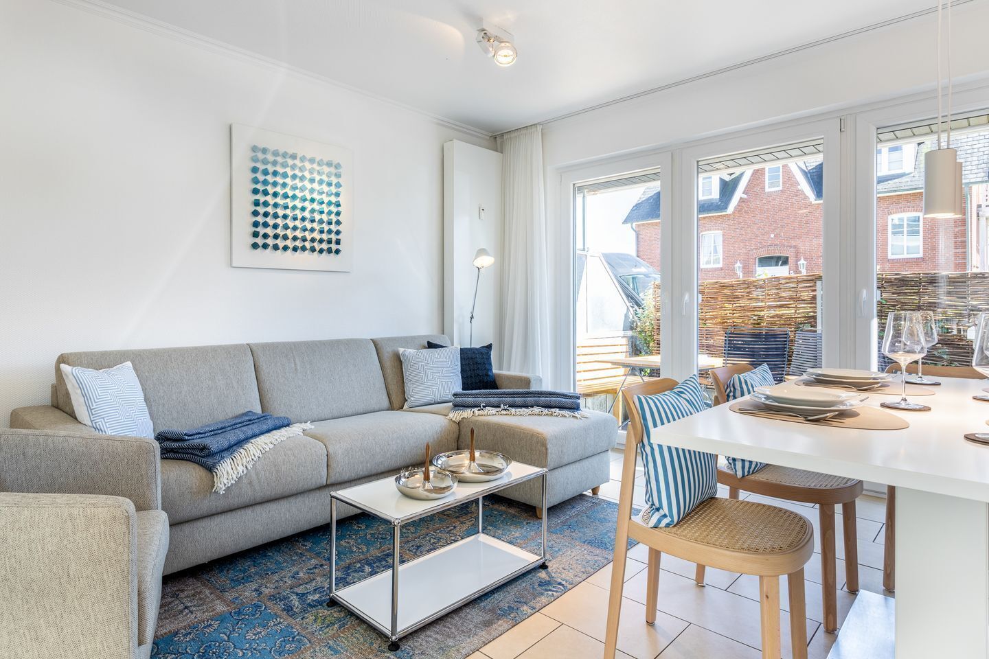 A modern living room with a grey sofa, a glass coffee table, and a dining area with a white table and chairs.