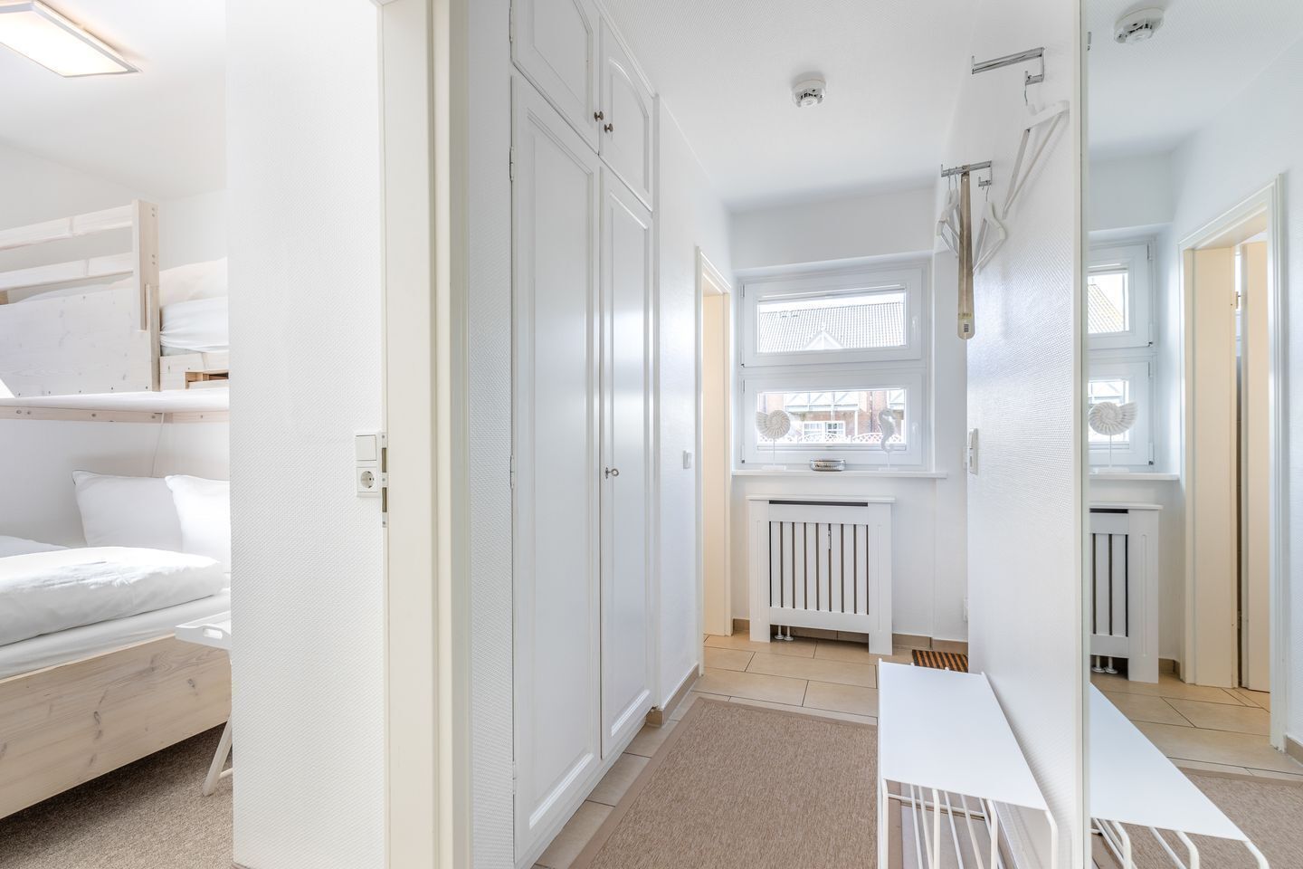 Une chambre avec un lit superposé, une armoire blanche, un radiateur et une fenêtre donnant sur un beau paysage.