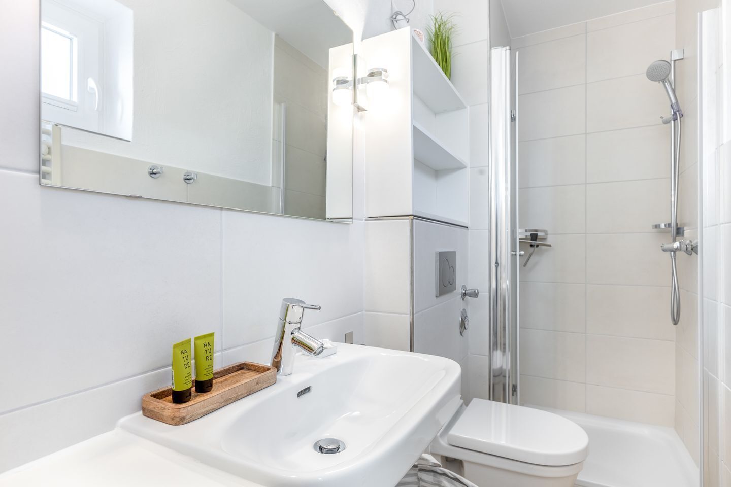 Une salle de bain moderne avec un lavabo blanc, des toilettes et une douche. On peut voir deux bouteilles vertes sur le lavabo.
