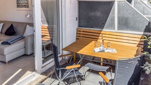 A modern outdoor seating area with a wooden table and metal chairs, a glass door leading to a living room, and a blackboard on the wall. - Ringelgans - Urlaub im Herzen von Westerland, das Erleben Sie in dem Appartement Ringelgans (Sylt)