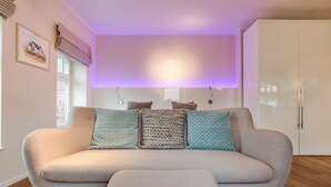 Un salon moderne avec un canapé et un pouf, un meuble blanc et un luminaire fixé au mur.