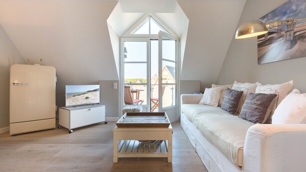 Une chambre de style loft moderne, dotée d’une grande lucarne, d’un canapé blanc, d’une petite table et d’un réfrigérateur.