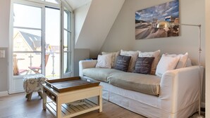 Un salon chaleureux avec un canapé blanc, une table basse en bois et une grande fenêtre donnant sur l’extérieur.