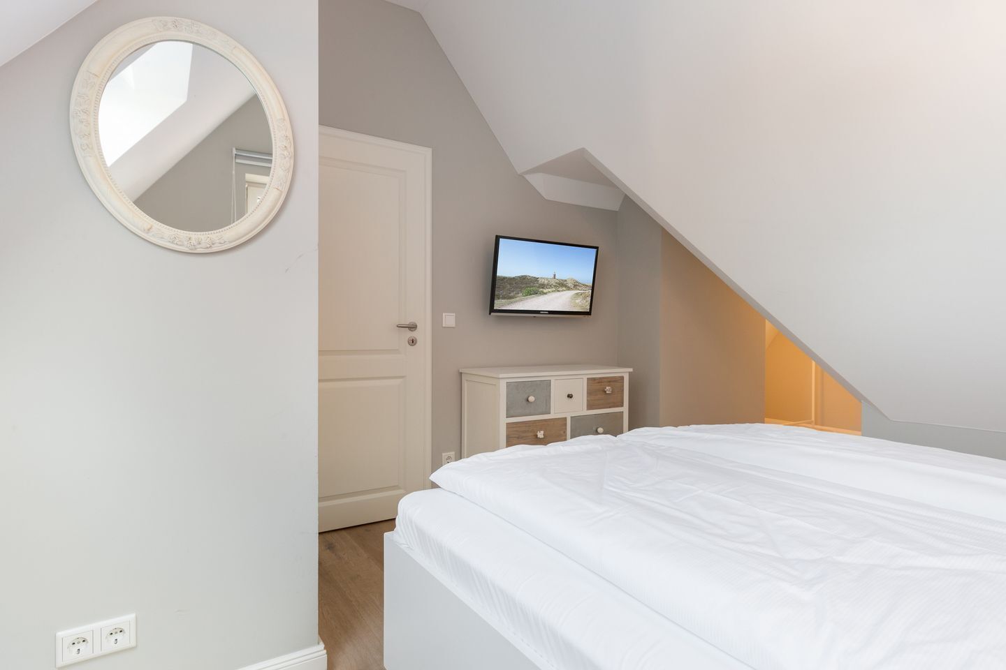 A bedroom with a bed, a dresser, a television mounted on the wall, and a door.