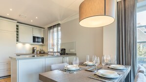 Une cuisine moderne avec des meubles blancs, un coin repas doté d’une table en bois pour six personnes et une grande fenêtre agrémentée de rideaux.