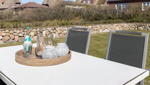 Une table sur laquelle est disposée une collection d’objets décoratifs, deux chaises en métal ajouré et, au fond, un mur en pierre.