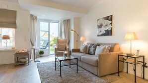 A modern living room with a sofa, armchairs, a coffee table, and a side table with a lamp. - Dünen & Meer, App. 2 Dünen-nest - In Strandnaher und Dennoch Zentraler Lage Gelegenes 3-raum (Sylt)