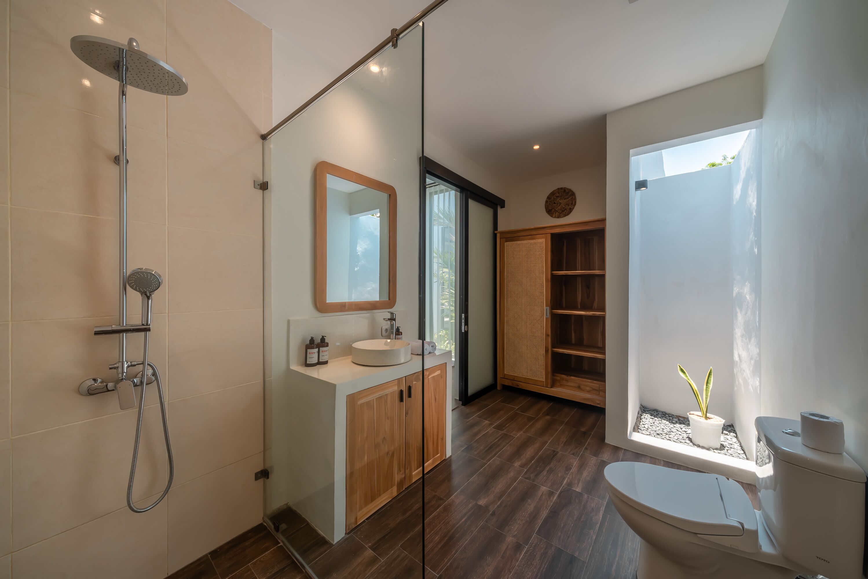 A modern bathroom with a glass shower enclosure, a wooden vanity, a large mirror, and a toilet with a window view.