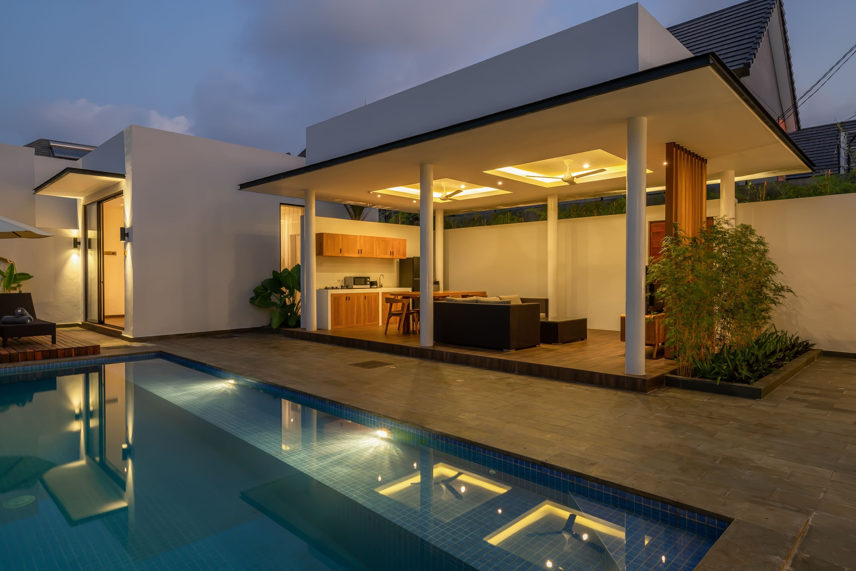 Et moderne hus med swimmingpool, udendørs køkken og en overdækket terrasse.