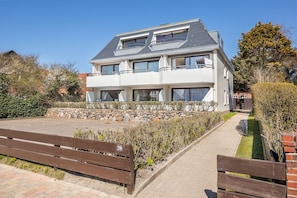 Une maison à deux étages avec un mur de soutènement en pierre, une allée pavée et un banc en bois.