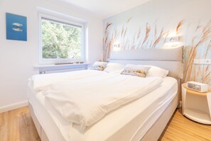 Una camera da letto con un letto grande, un comodino con una radio, una finestra che si affaccia sul verde e un murale raffigurante un campo di grano.