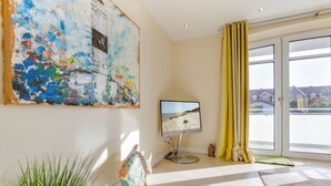 Una sala de estar moderna con un cuadro abstracto grande, un televisor de pantalla plana, una planta en maceta y vistas a través de una puerta corrediza de cristal.