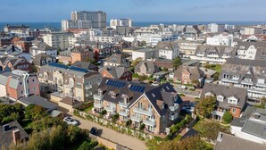 Zona residencial con casas, algunas con paneles solares, y vista al mar de fondo.