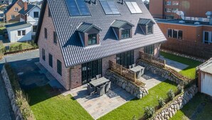 Une maison moderne dotée d’un toit en pente, de grandes fenêtres et d’un patio aménagé avec du mobilier d’extérieur.