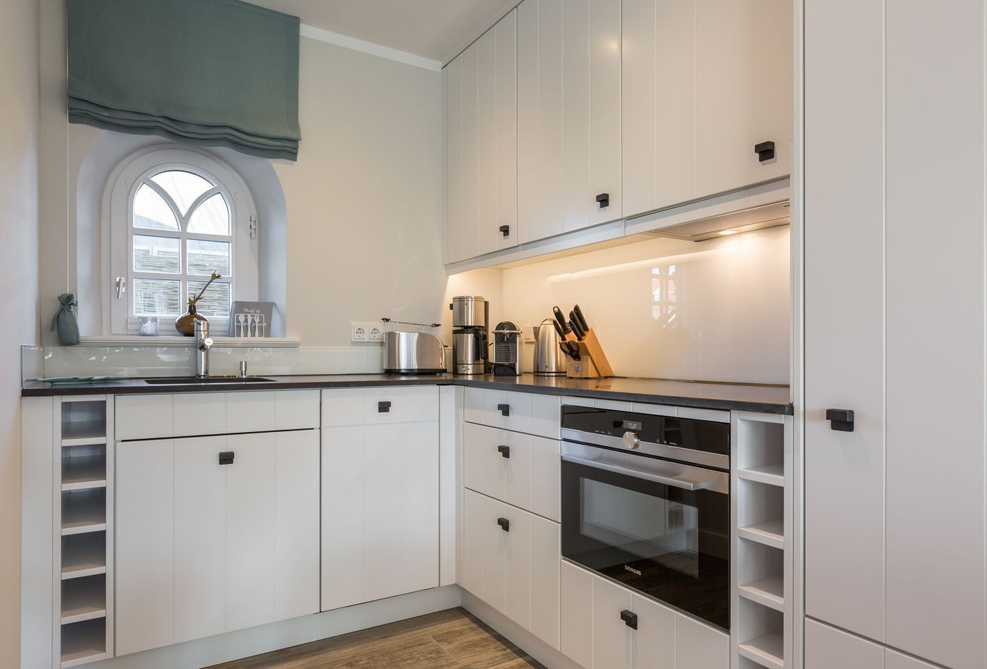 Cozinha moderna com armários brancos, forno embutido e janela com vista.