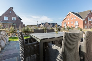 Une terrasse extérieure avec une table et des chaises en osier, entourée de murs en pierre et offrant une vue sur des immeubles résidentiels.