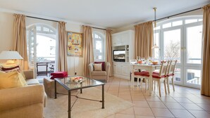 A spacious living room with a sofa, a glass coffee table, and a dining area with chairs and a table. - Nette-star, App. 14 - Einmalige Lage. Fantastischer Wellnessbereich. Viel Platz und Stil für Zwei (Sylt)