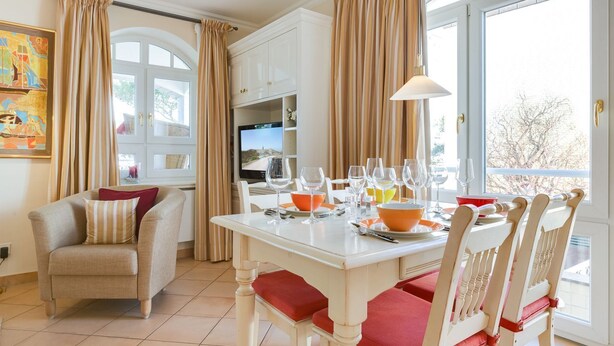 A dining area with a table set for six, a sofa, and a television in the background. - Nette-star, App. 14 - Einmalige Lage. Fantastischer Wellnessbereich. Viel Platz und Stil für Zwei (Sylt)