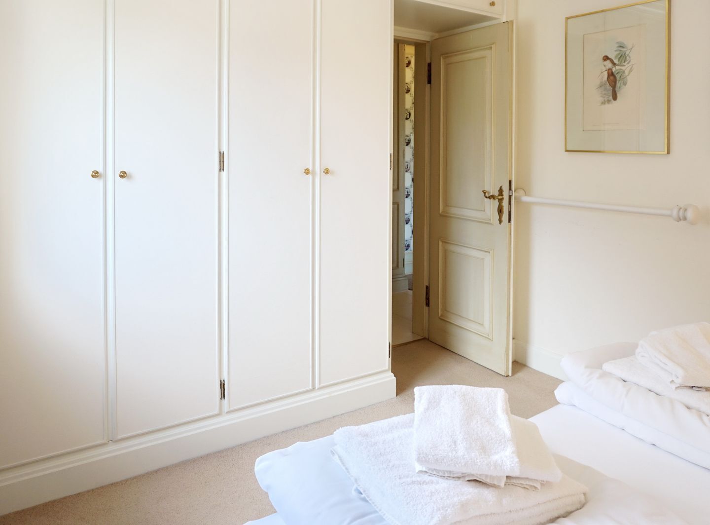 A bedroom with a large wardrobe, a bed with neatly folded white towels, and a framed picture on the wall.