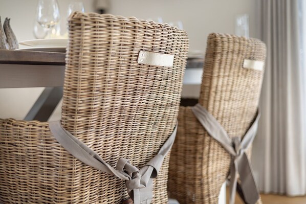 Des chaises en osier, ornées de rubans gris noués autour des dossiers, sont disposées autour d’une table à manger.